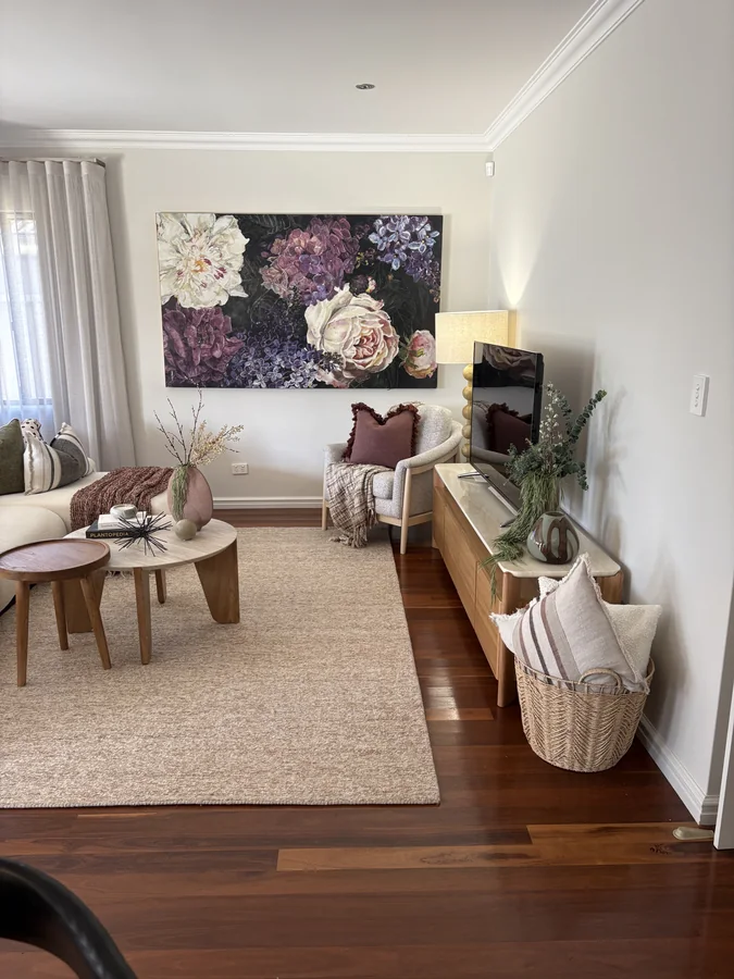 Styled living room with floral artwork, plum accents, natural timber and decorative greenery
