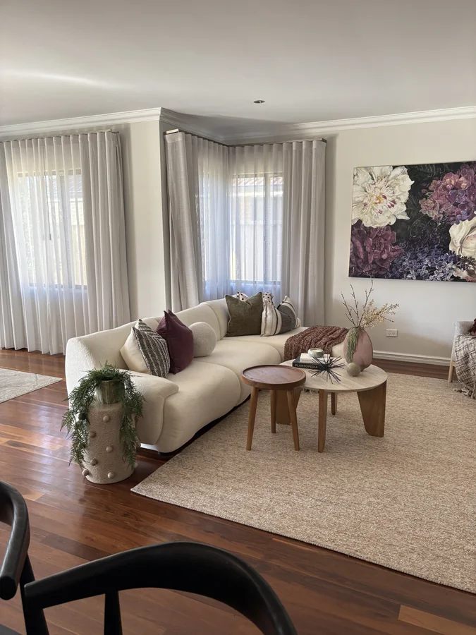 Curved ivory sofa with plum and green cushions, timber coffee tables and floral artwork