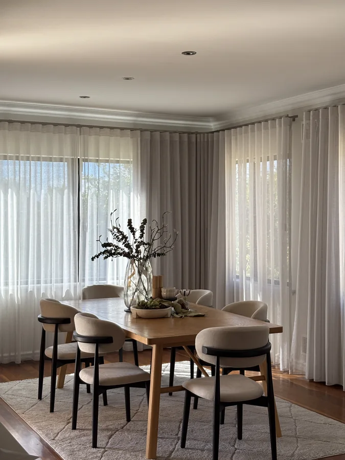 Timber dining table with cream chairs, a glass vase and sheer curtains
