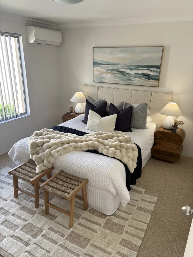 Bedroom with ocean artwork, navy bedding, textured cream throw and sculptural timber bedside tables