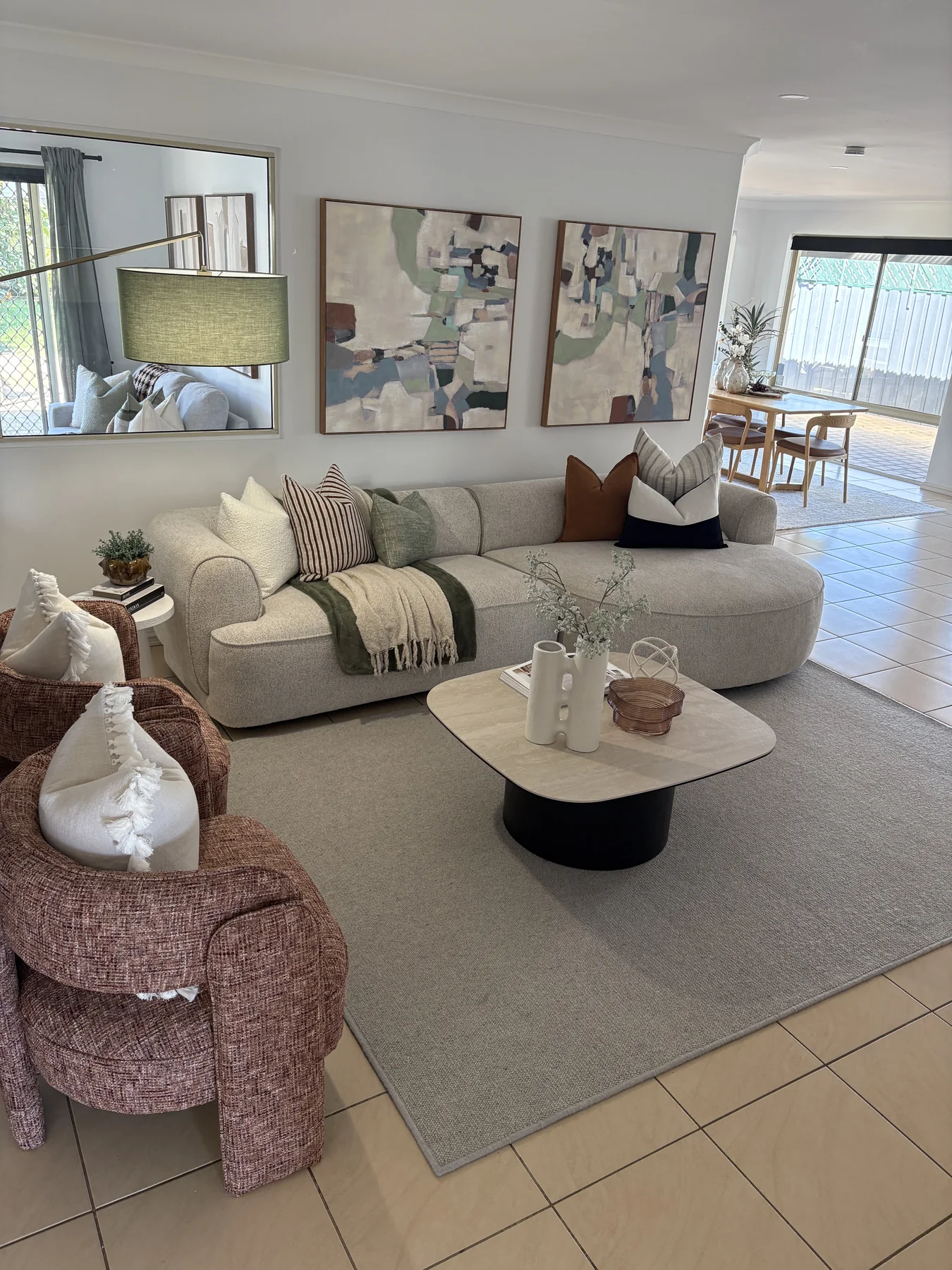A styled living room with a curved cream sofa, textured armchairs, green accents and abstract artwork