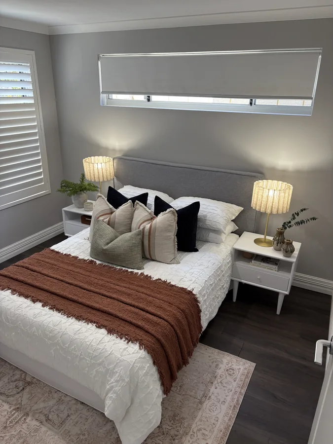 Bedroom with a rust throw, layered cushions and warm woven bedside lamps