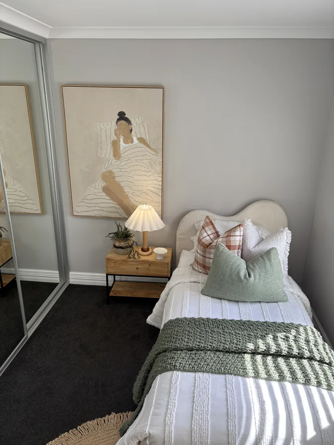 Single bedroom with a curved headboard, sage throw, checked cushion and pleated lamp