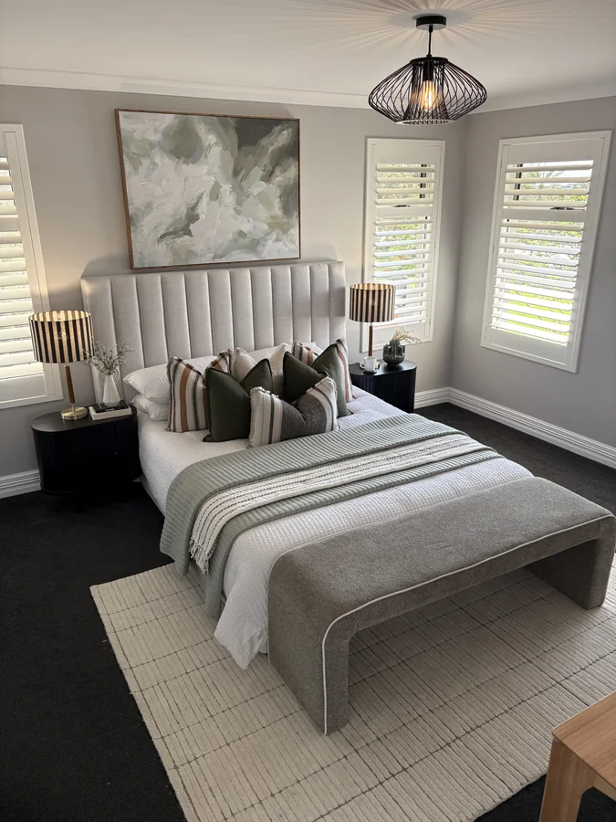 Bedroom with a tall upholstered headboard, sage bedding, striped lamps and a bench
