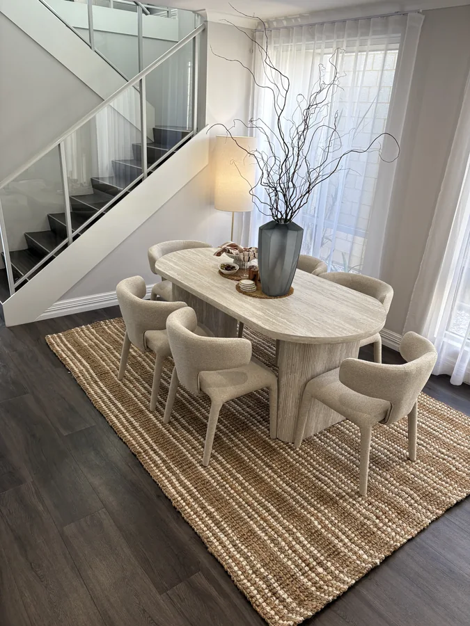 Oval stone-look dining table with upholstered chairs, a tall vase and woven rug