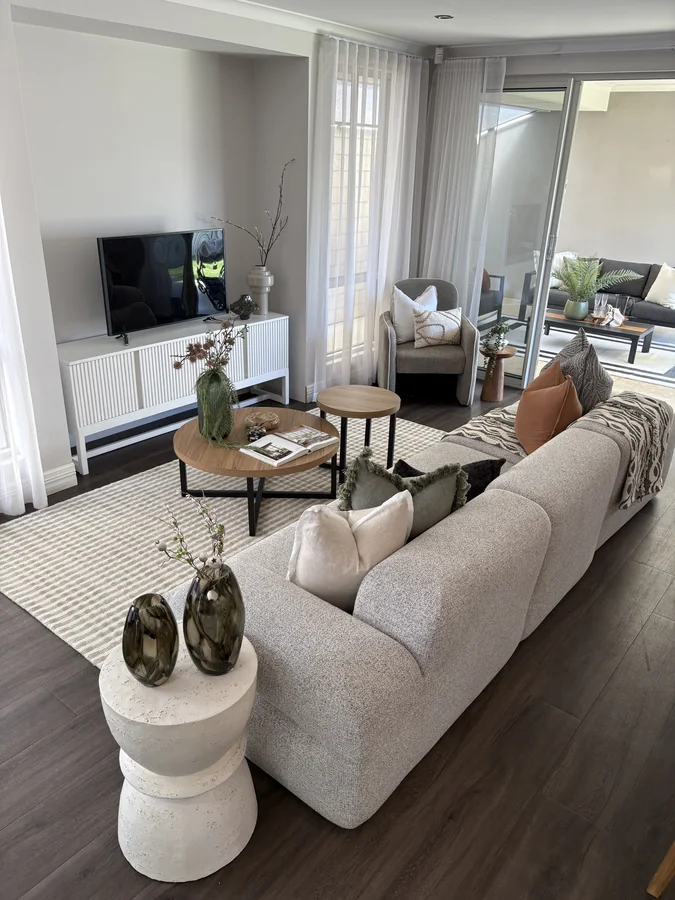 Open living room with a textured sofa, timber nesting tables and sheer curtains
